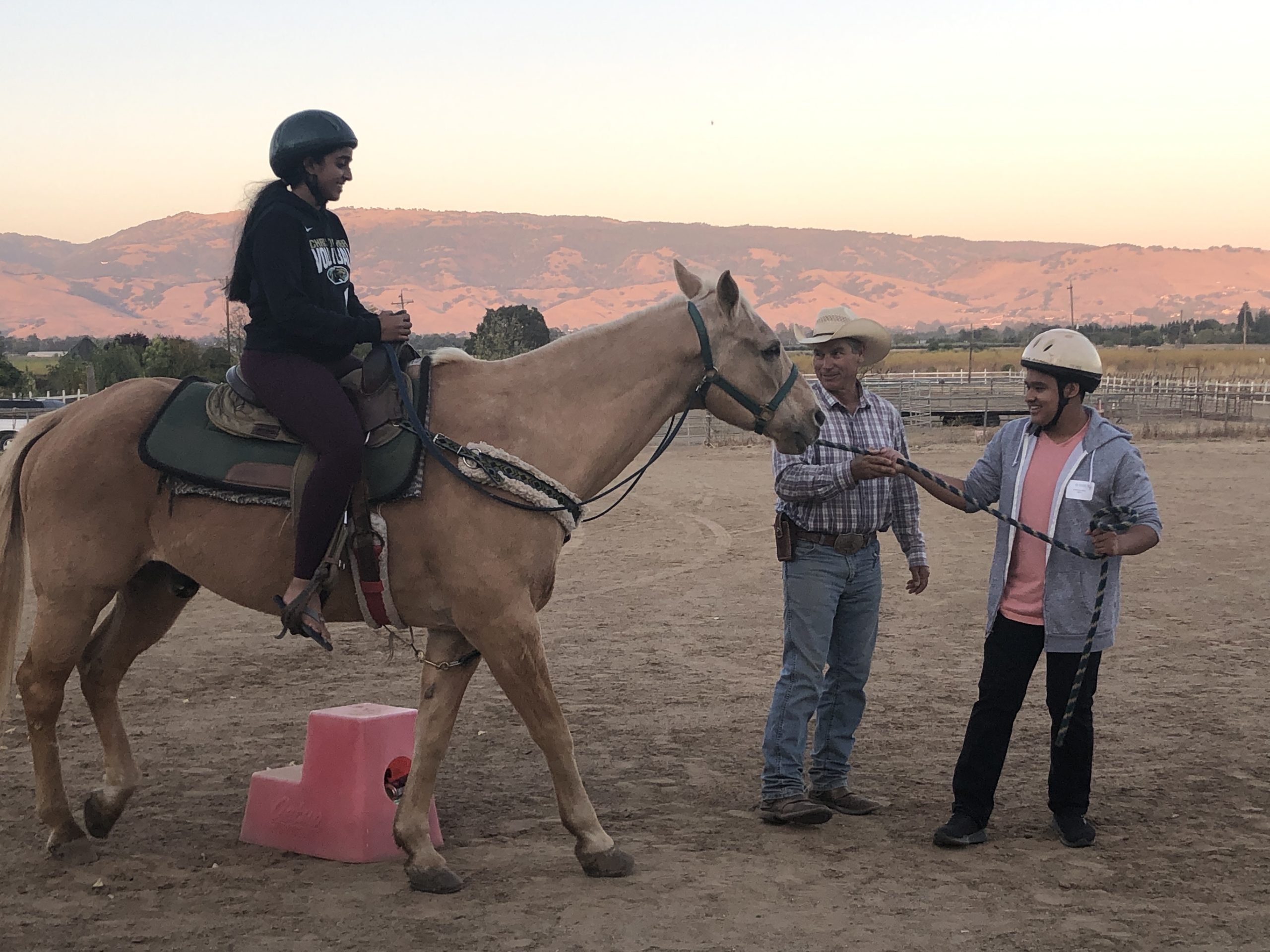 pair of younger people riding a horse with an instructor helping